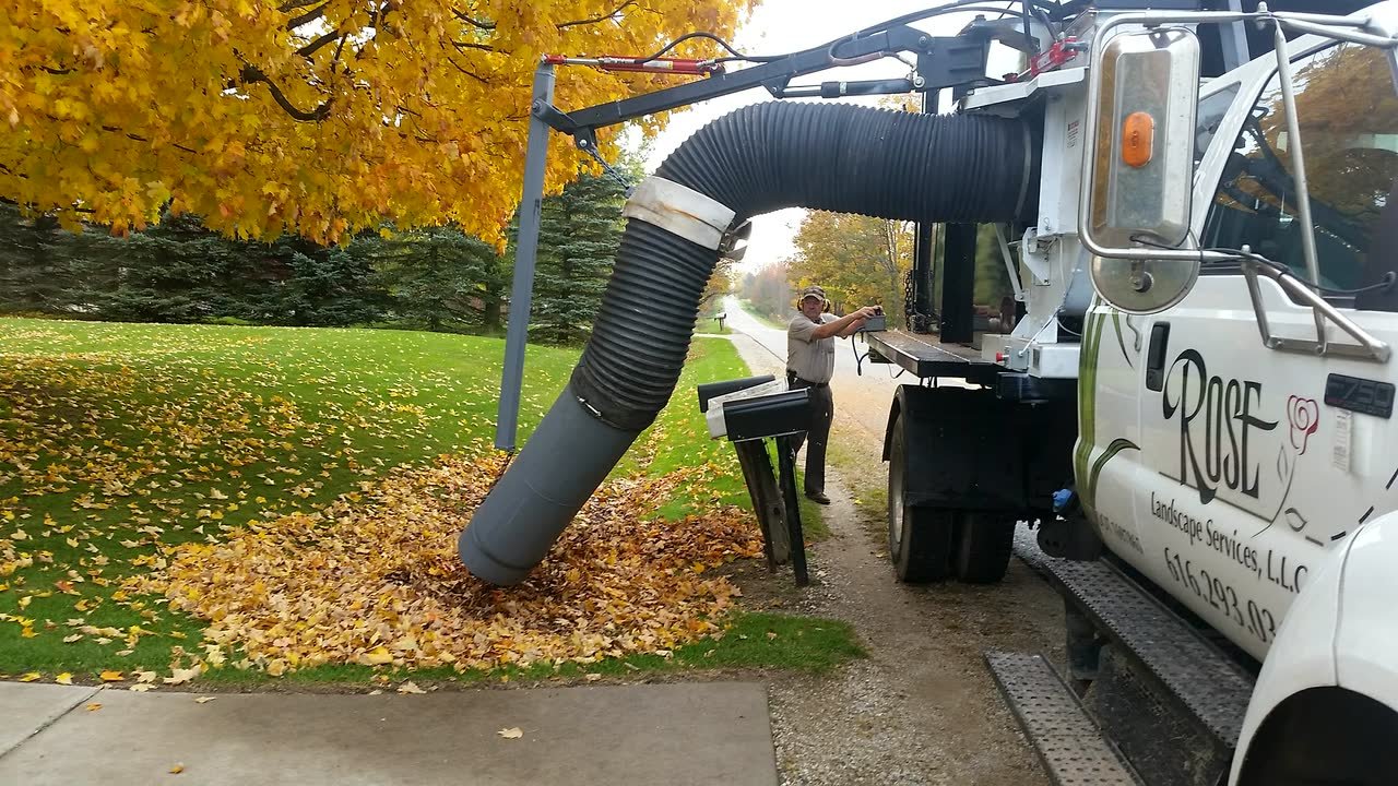 Rose's vacuum truck collecting leaves beside a roadside pile under a yellow maple